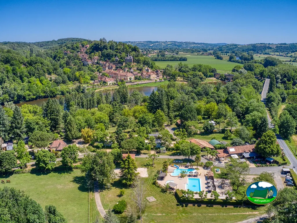 vista aérea del camping junto al río con piscina, bungalós y el pueblo medieval de Limeuil al fondo