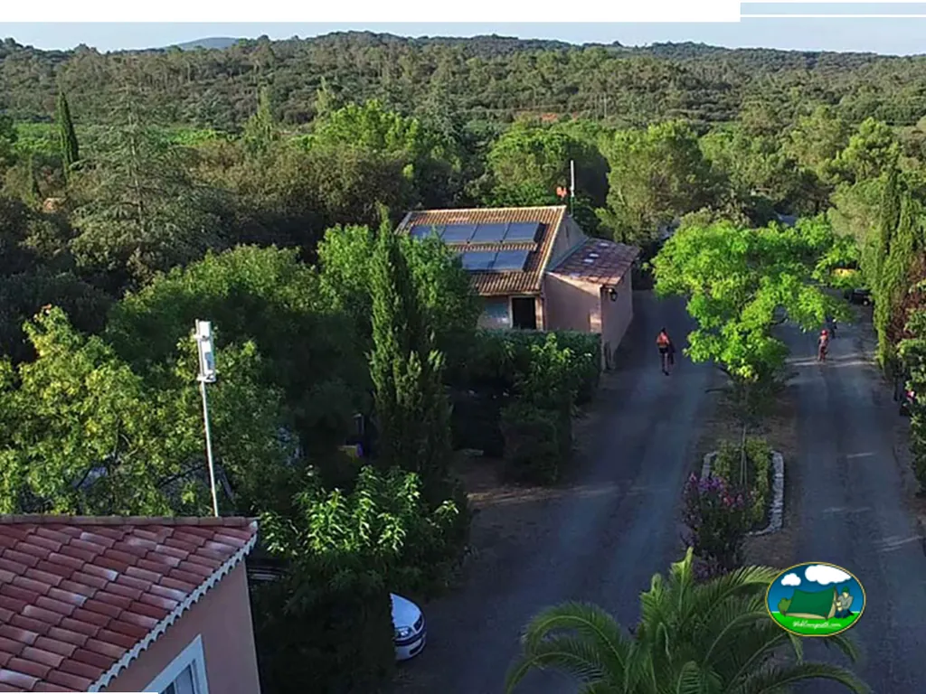 vista aérea del camping con viales arbolados, chalet con placas solares y paseantes