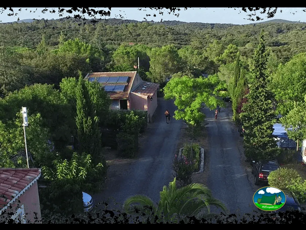 vista aérea del vial arbolado del camping con ciclistas y chalet con placas solares