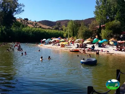 Río con playa, bañistas y sombrillas, montaña al fondo del Camping Los Molinos, Sanlúcar de Guadiana (Huelva)