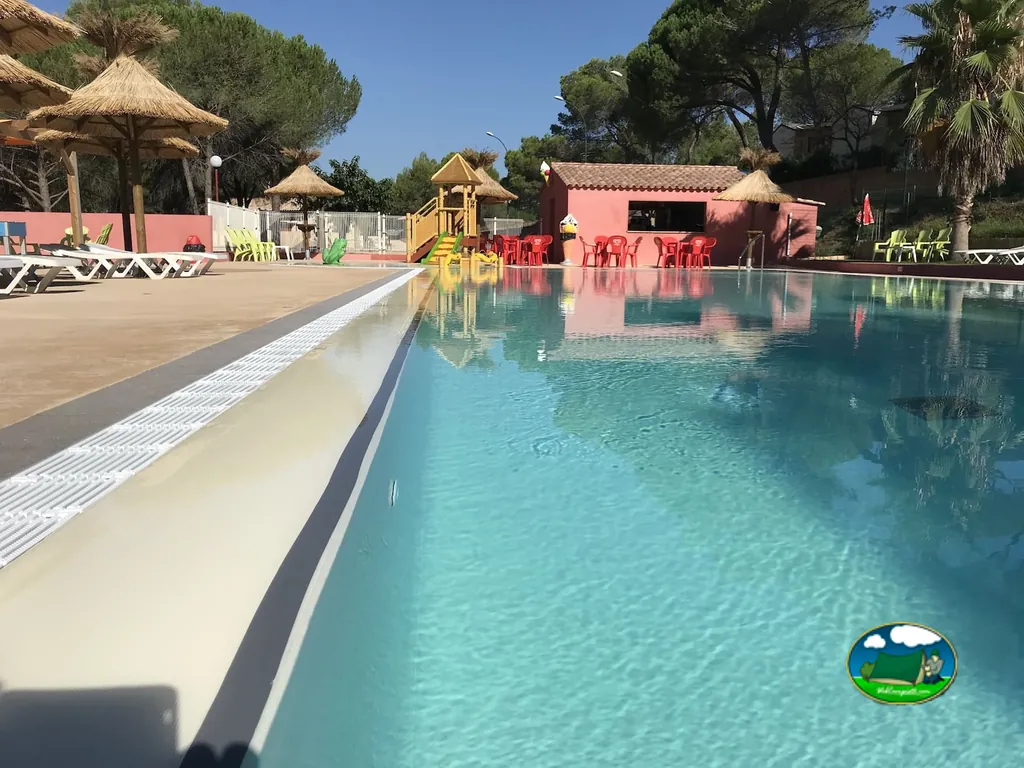 piscina con sombrillas de paja, bar y zona infantil junto a palmeras en Roquebrune-sur-Argens