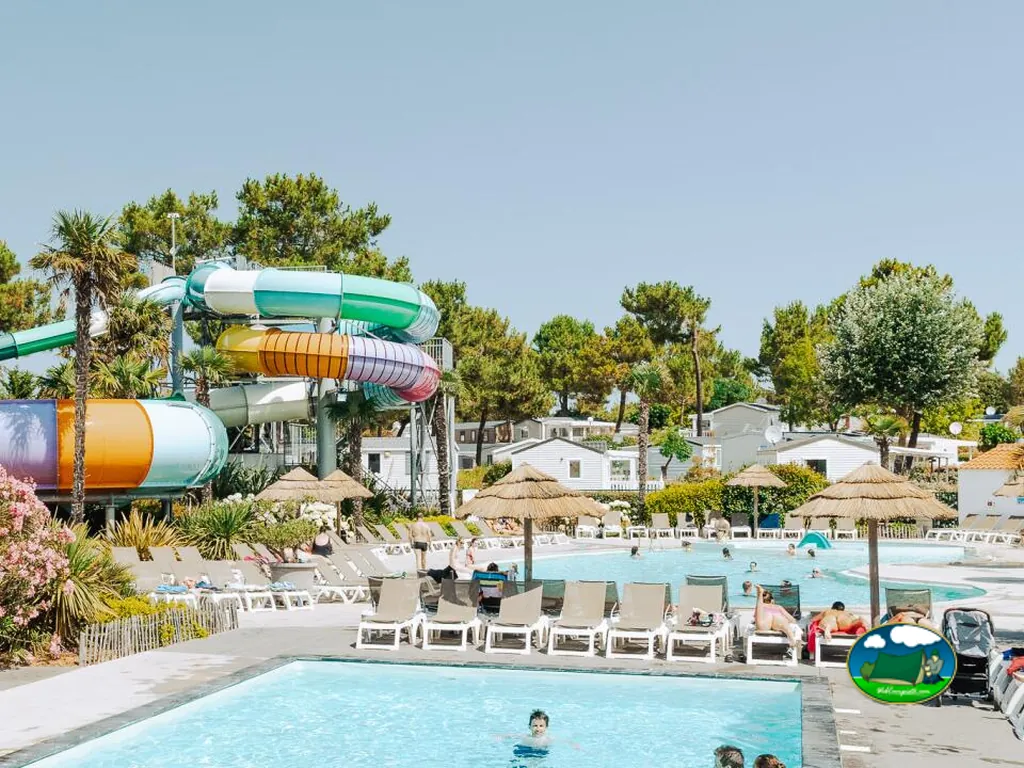 piscina con toboganes de colores y mobil-homes al fondo entre palmeras en Saint-Jean-de-Monts