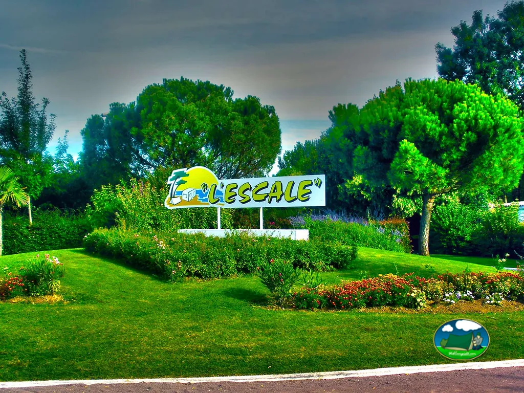 cartel de entrada 'L'Escale' rodeado de jardín con flores bajo cielo dramático en Meschers-sur-Gironde