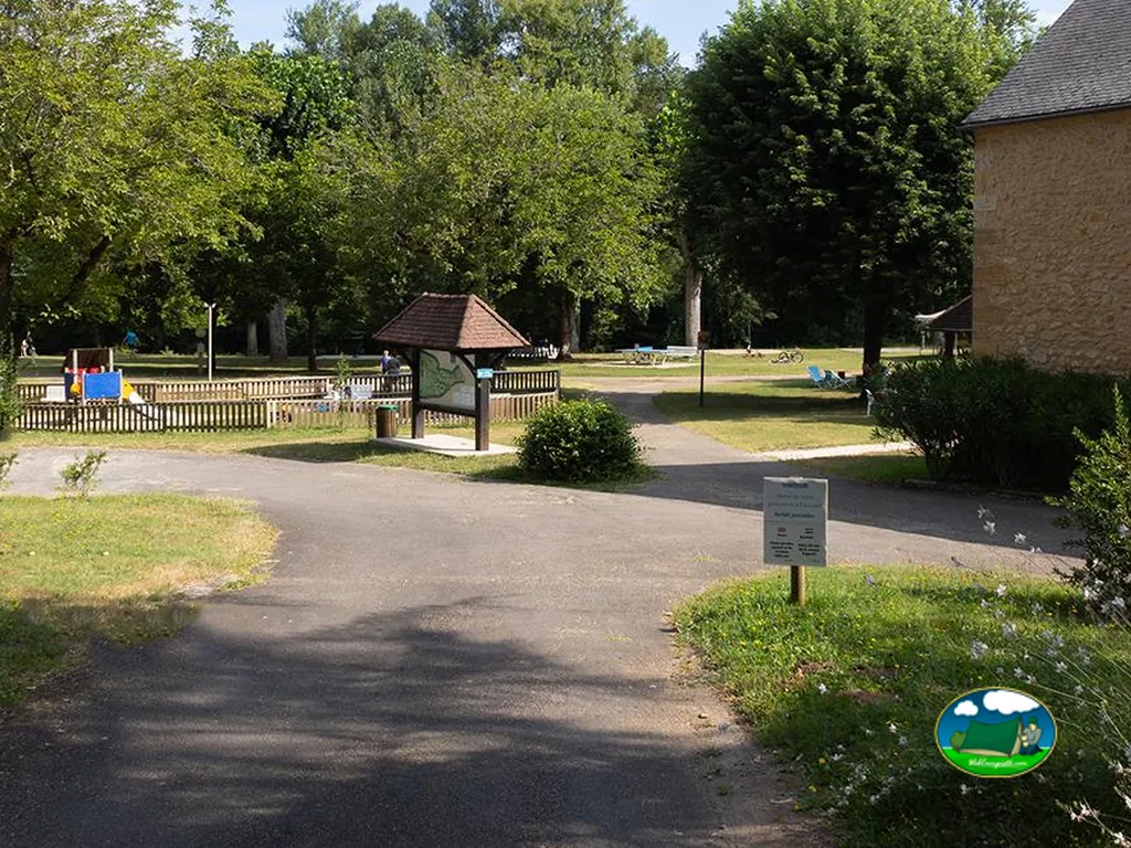 senderos del camping con zona infantil y panel informativo entre árboles en Domme