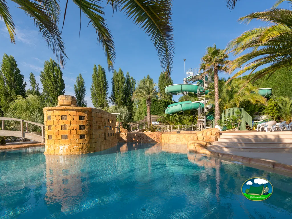 piscina con torreón de piedra decorativo, toboganes verdes y palmeras en Saint-Georges-d'Oléron
