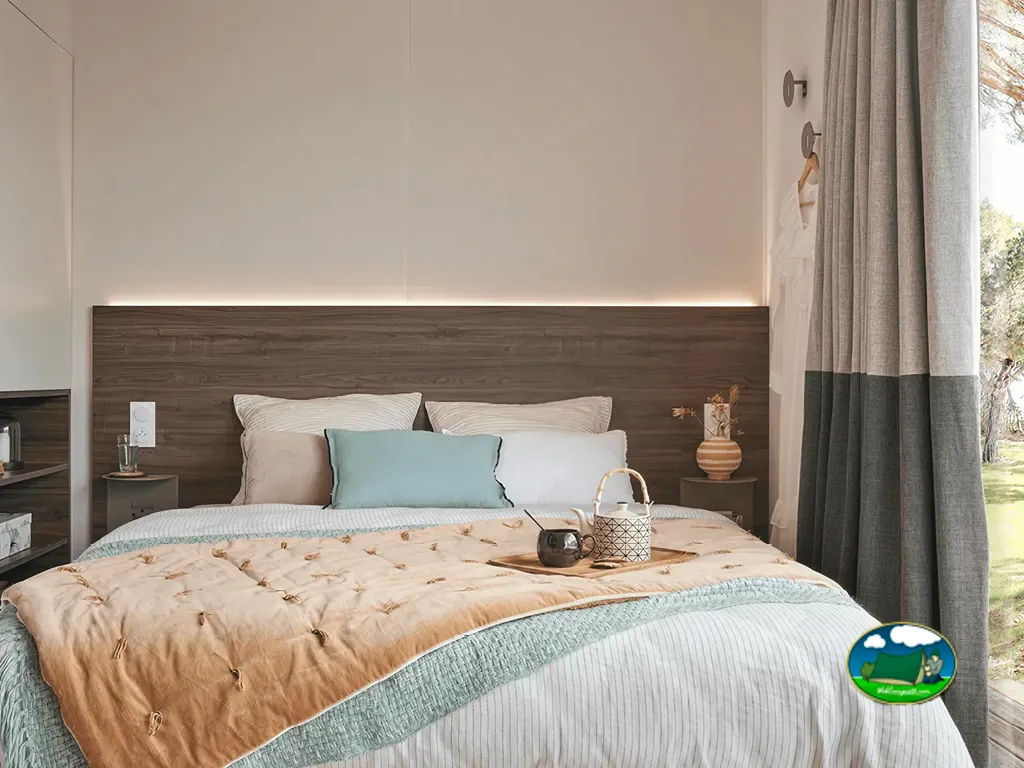 dormitorio de mobil-home con cabecero de madera iluminado y bandeja de té sobre la cama