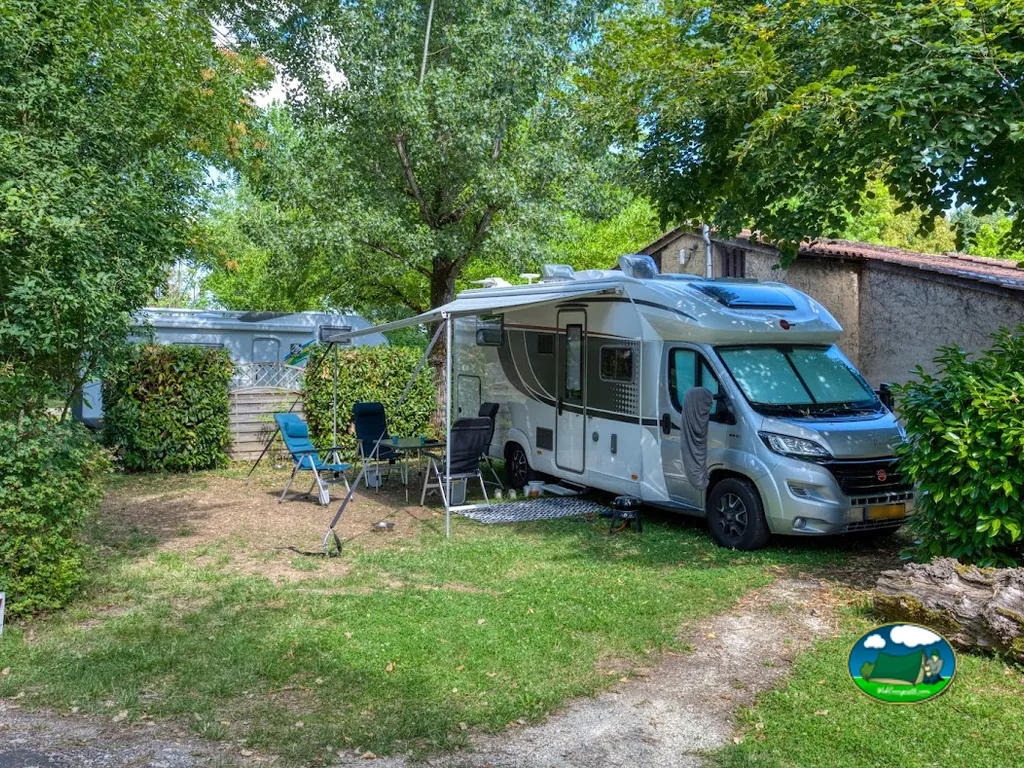 autocaravana estacionada en una parcela sombreada con mesa y sillas en el camping de Domme