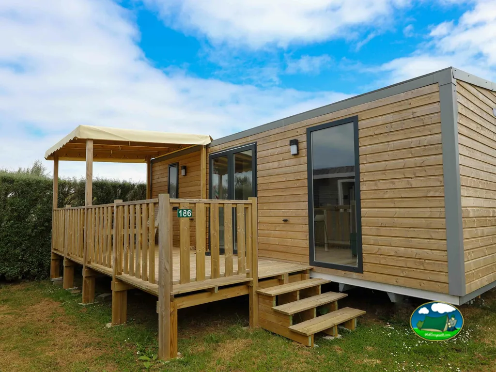 exterior de un mobil-home de madera con terraza numerada bajo un cielo con nubes