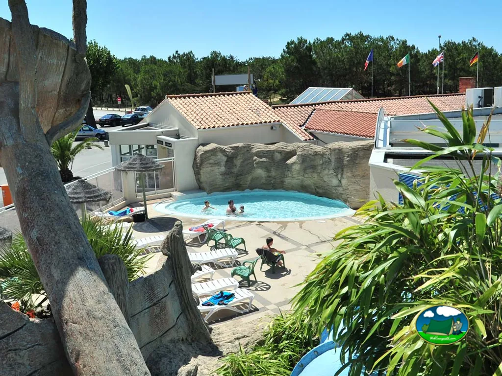 piscina con jacuzzi rodeado de rocas artificiales y banderas junto al aparcamiento del camping