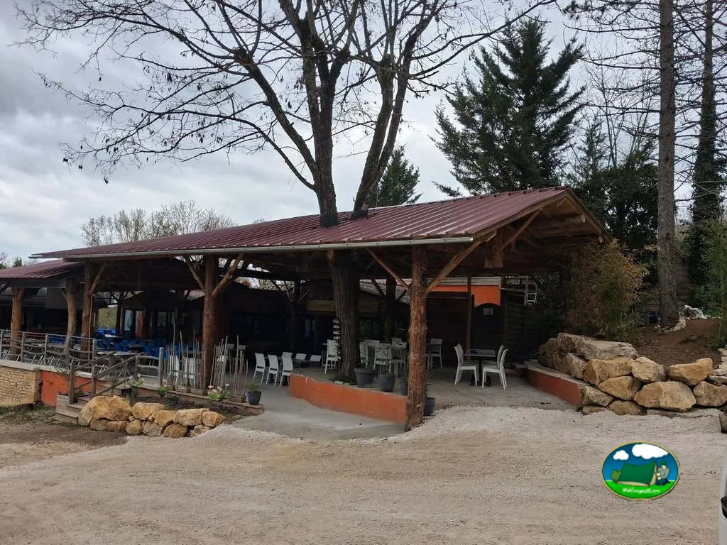 porche cubierto con mesas y sillas del bar-restaurante del camping bajo un cielo nublado