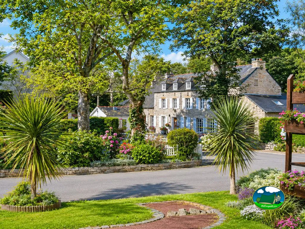 fachada de piedra de la casa señorial con jardín de flores y palmeras del camping en La Forêt-Fouesnant