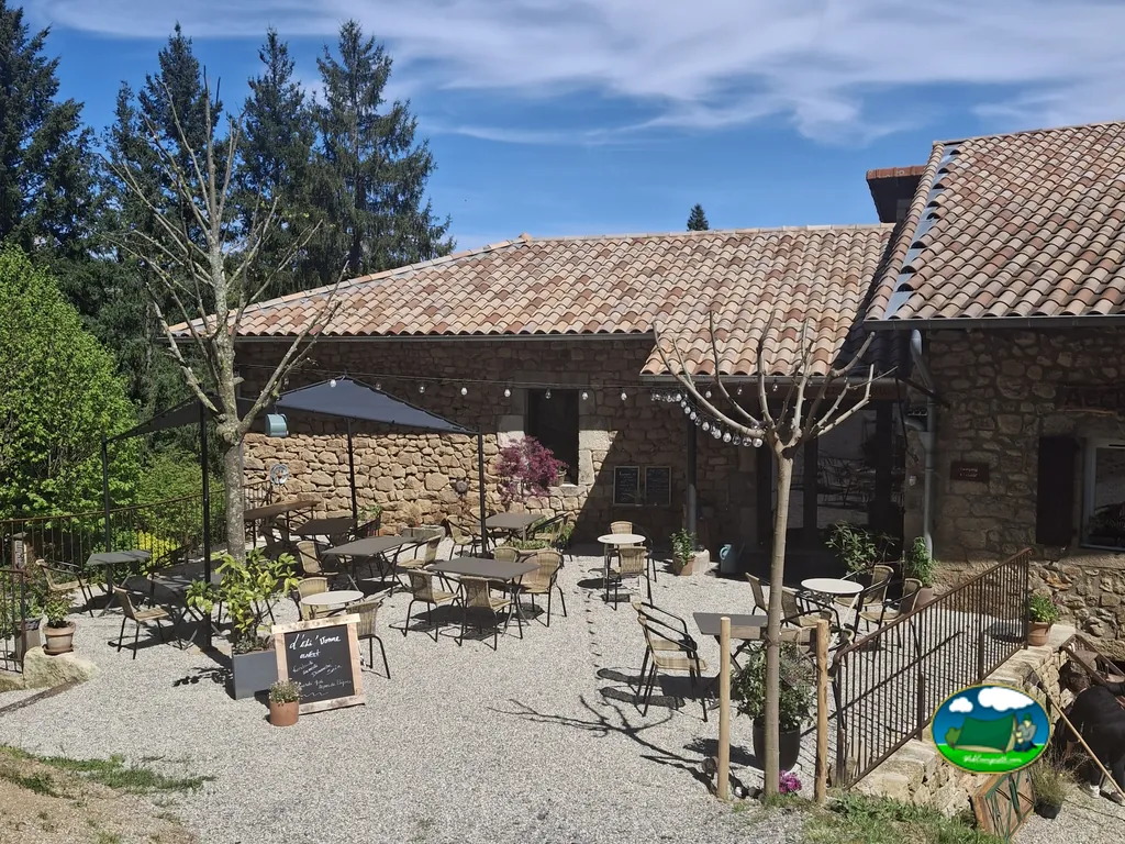 terraza exterior de piedra con mesas y sombrillas del restaurante del camping en Fabras