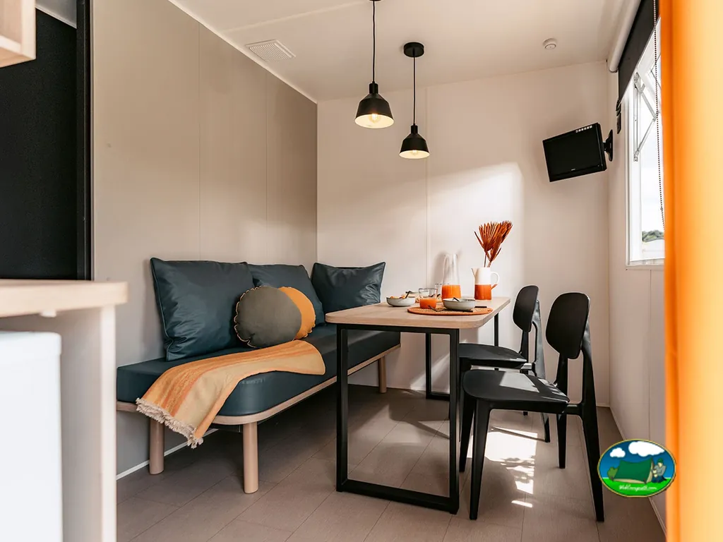 comedor de un mobile home con sofá azul, mesa de madera y decoración naranja