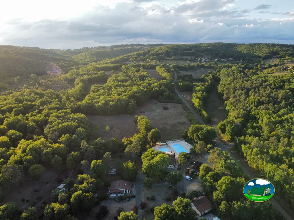 vista aérea de la piscina y los edificios del camping rodeados de bosque al atardecer en Tourtoirac