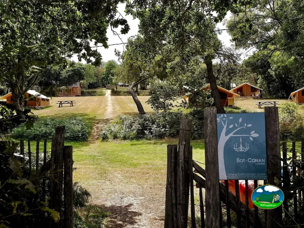 sendero de entrada hacia las tiendas lodge del camping junto a un cartel de acceso en Fouesnant