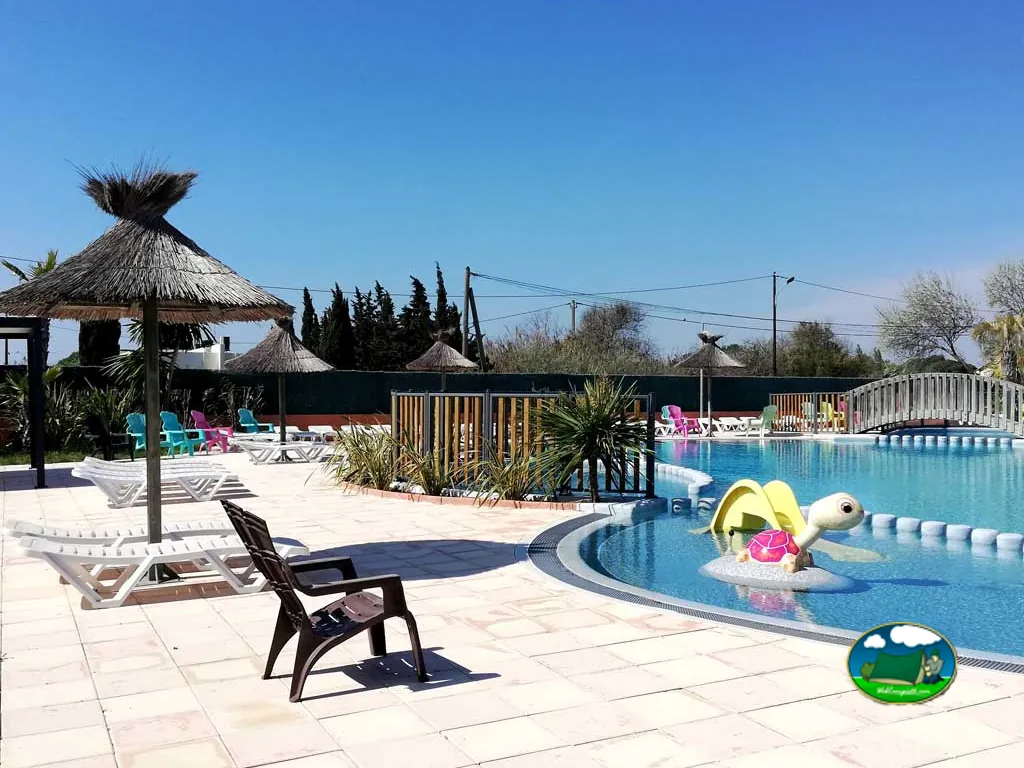 piscina infantil con tobogán en forma de tortuga y hamacas bajo sombrillas de paja en Marseillan