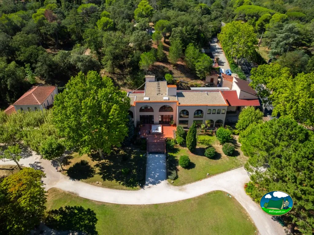 vista aérea del edificio principal del camping rodeado de jardines y arbolado en Le Boulou