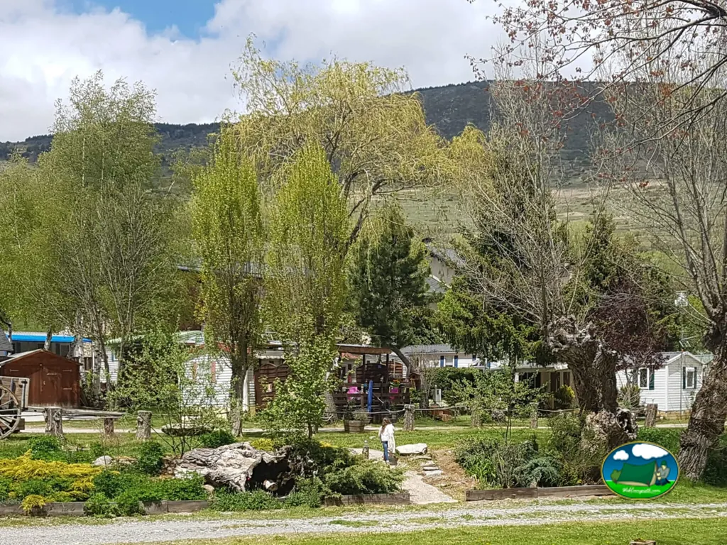 mobile homes entre árboles con las montañas al fondo y una persona paseando por el camino en Targassonne