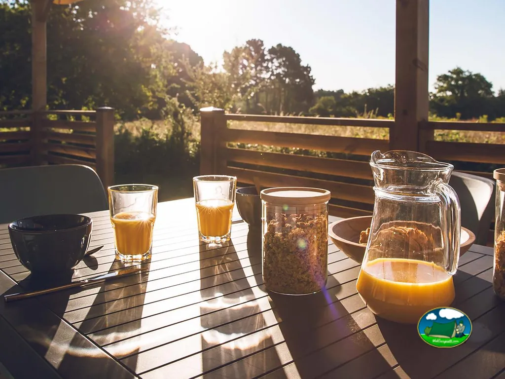 mesa de desayuno con zumo y granola en la terraza de un alojamiento a contraluz