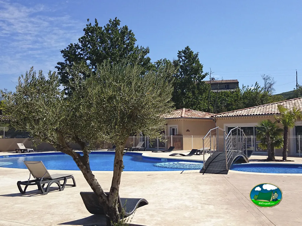 piscina con tumbonas y pasarela de madera junto al edificio principal del camping