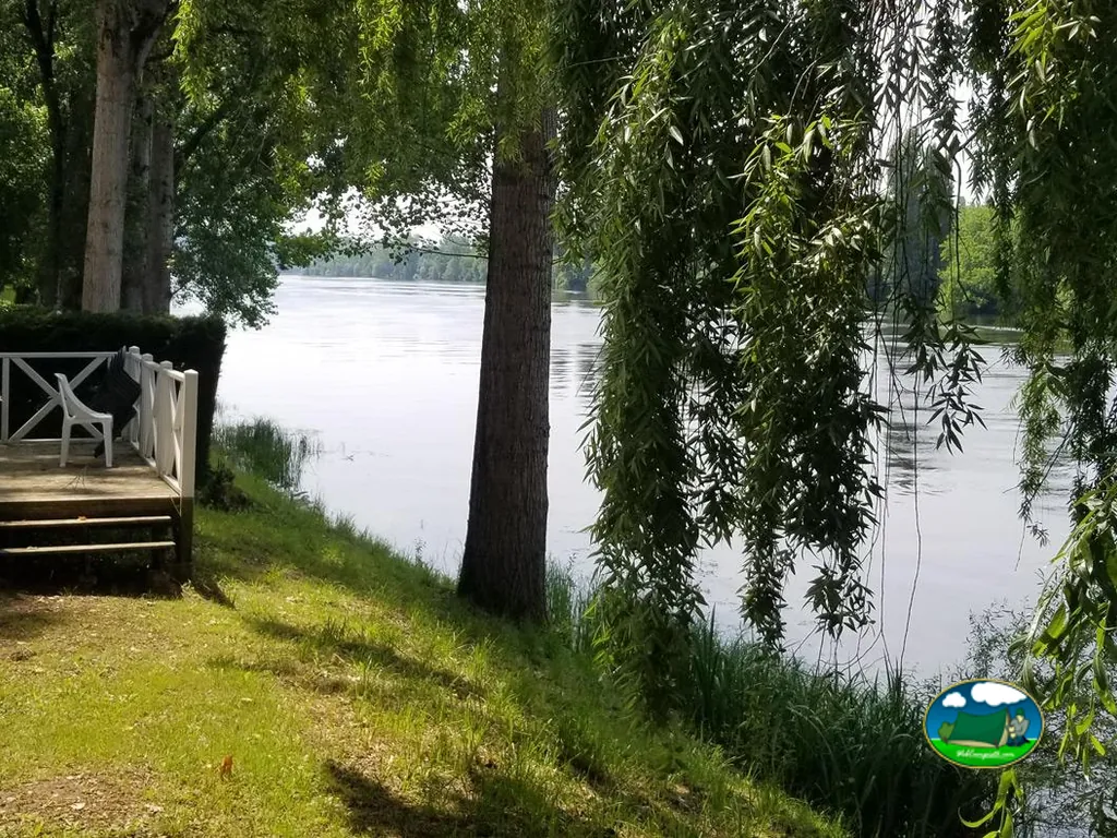 terraza de madera con silla junto al río bajo los sauces del camping
