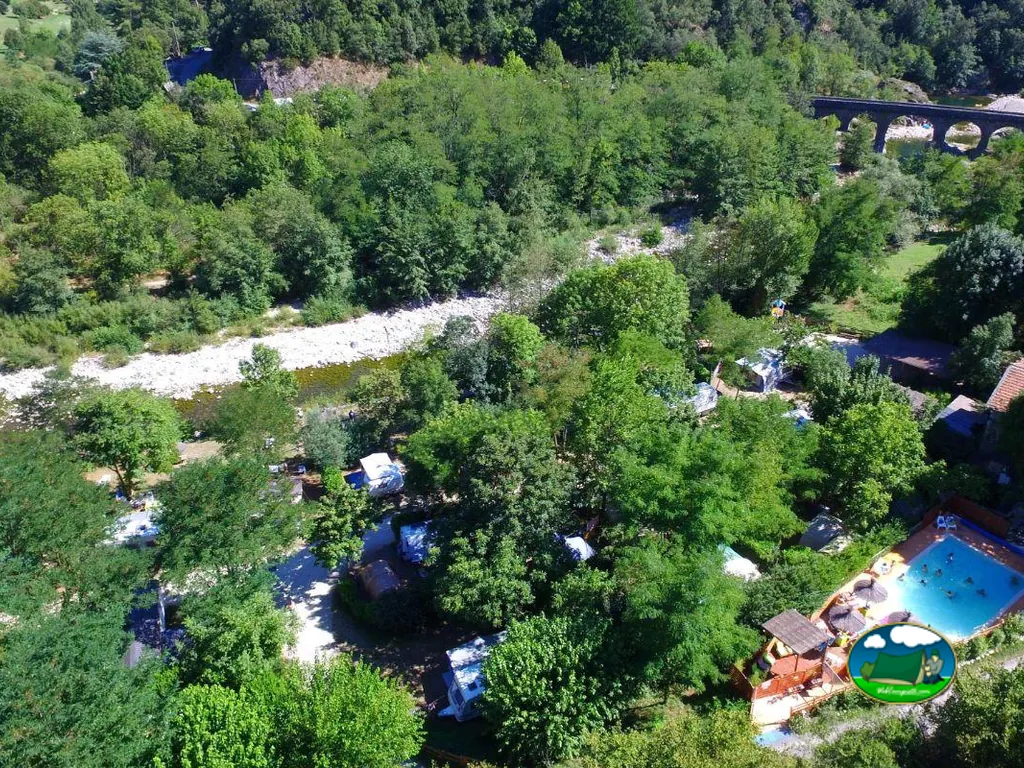 vista aérea del camping junto al río con piscina y parcelas arboladas en Meyras