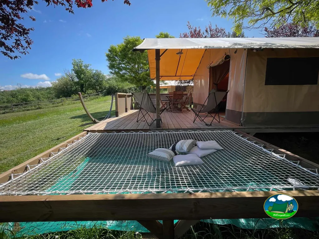 tienda de glamping con terraza de madera y una red hamaca con cojines en primer plano
