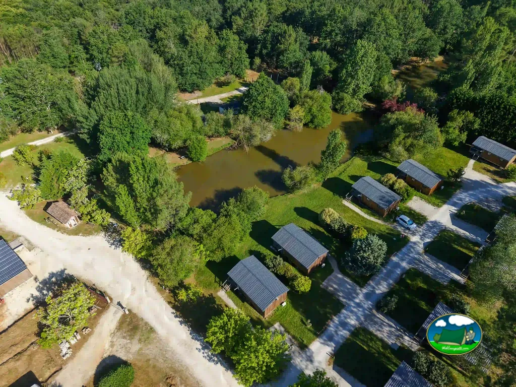 vista aérea de las cabañas del camping distribuidas junto a un camino y una laguna en Le Fouilloux