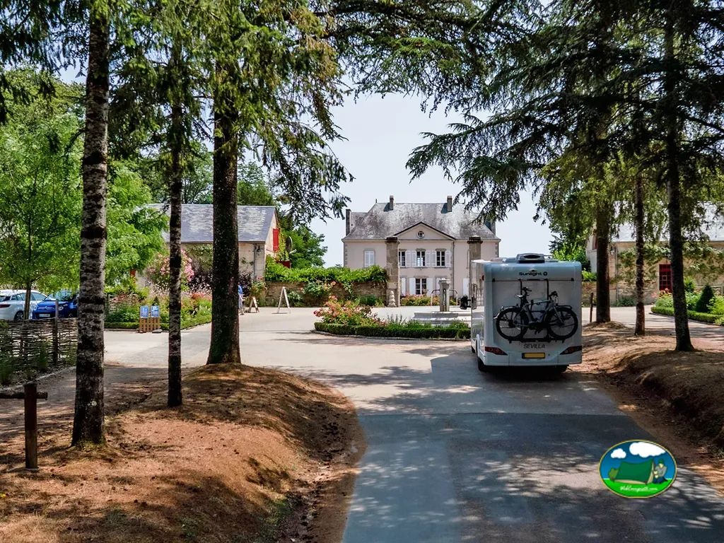acceso al camping con caravana y el castillo al fondo entre árboles en Saint-Julien-des-Landes