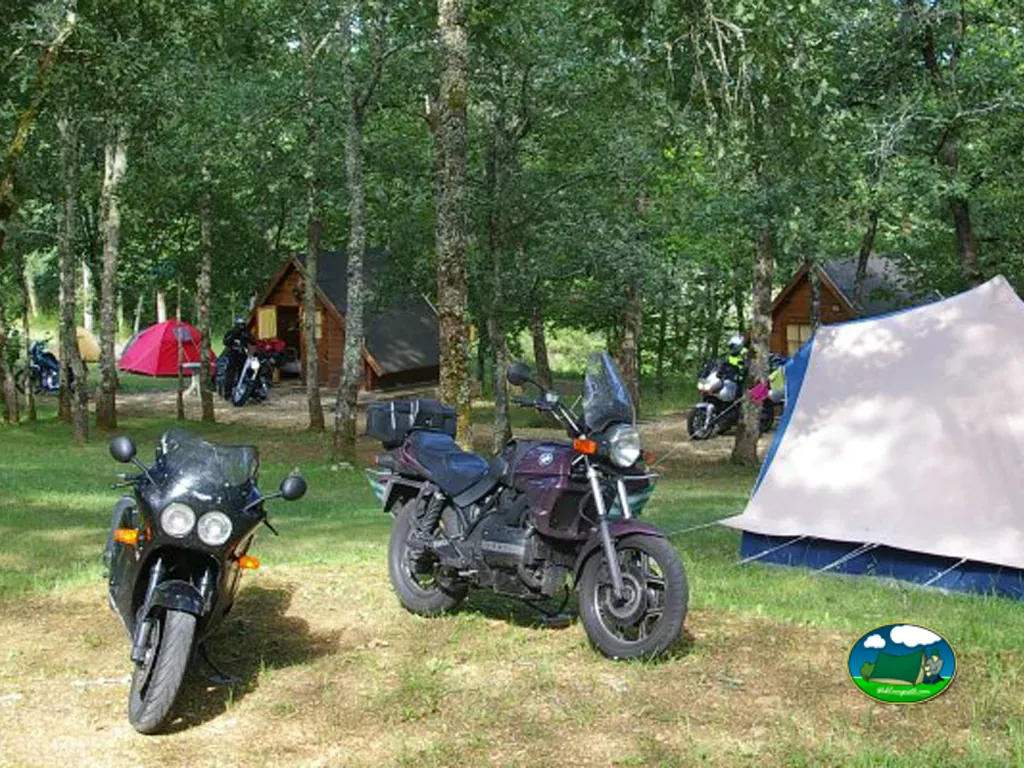 motocicletas aparcadas entre árboles junto a cabañas de madera y una tienda de campaña