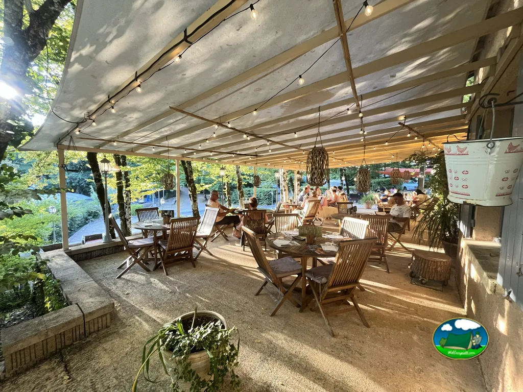 terraza cubierta con luces de guirnalda y mesas de madera bajo los árboles del camping