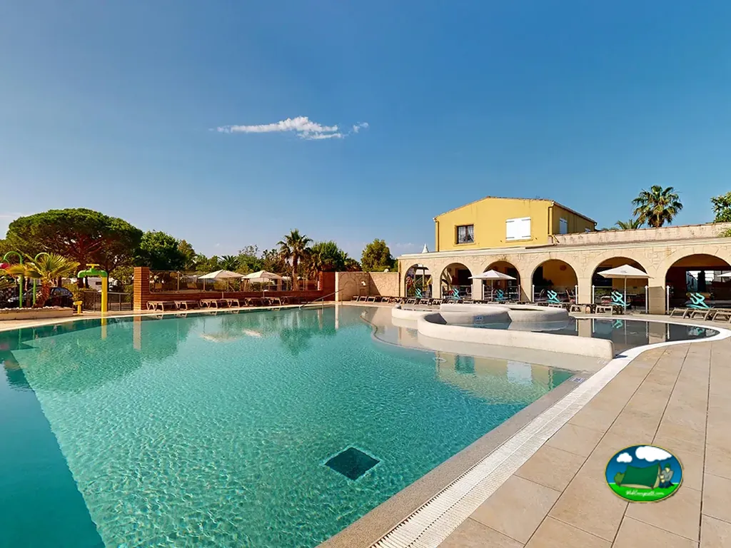 piscina del camping con edificio de arcos y tumbonas bajo sombrillas