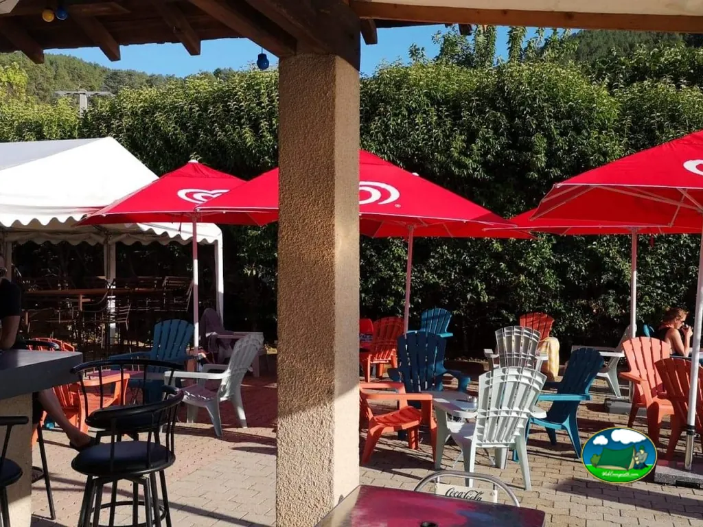 terraza del bar del camping con sombrillas rojas y sillas de colores