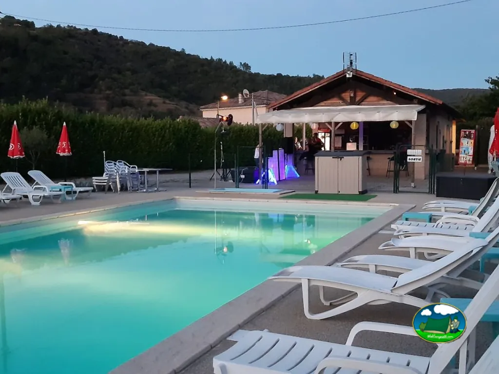 piscina del camping iluminada al atardecer con zona de bar y música en directo