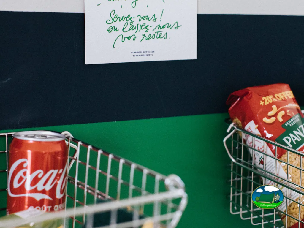 cestas de la compra con refrescos y pasta junto a un cartel de honestidad del camping