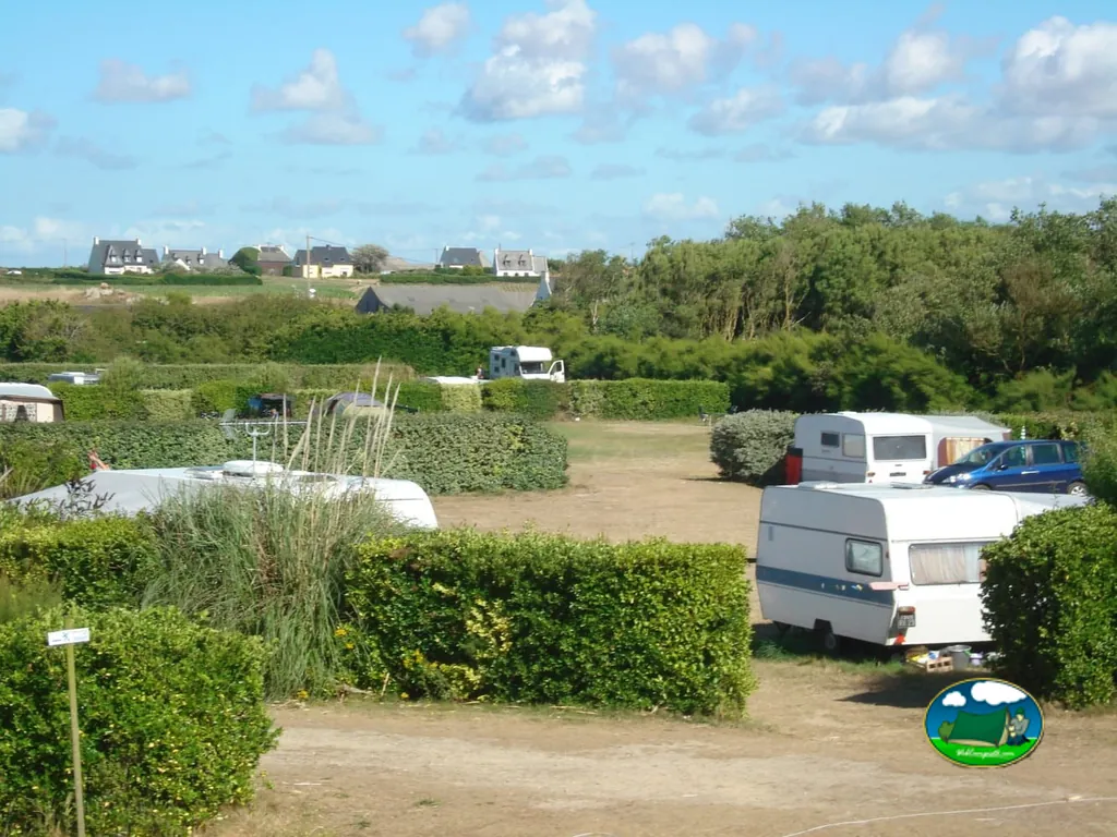 parcelas con caravanas separadas por setos y casas al fondo en Cléder