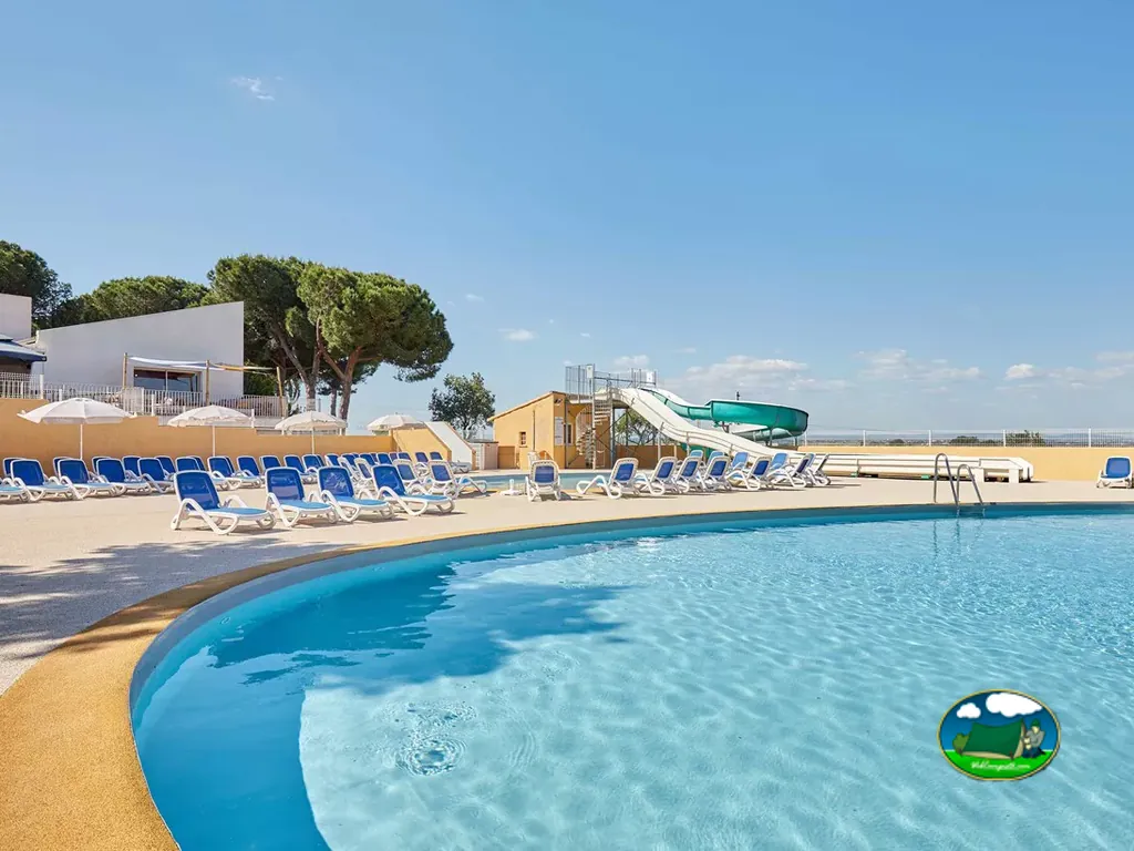 piscina exterior con tobogán acuático y tumbonas azules en Agde