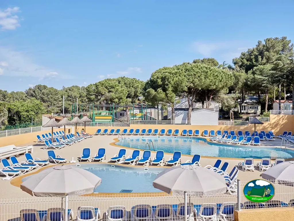 amplia piscina con parque infantil y hamacas azules rodeada de pinos en Agde