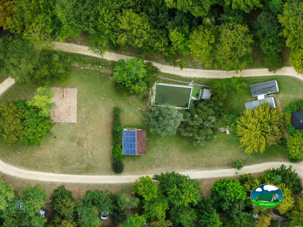 vista aérea del camping con piscina, edificios y placas solares entre árboles en Tursac