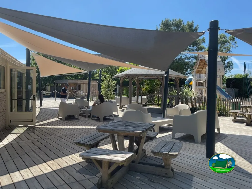 terraza cubierta con velas de sombra, mesas y zona infantil del camping en Château-d'Olonne