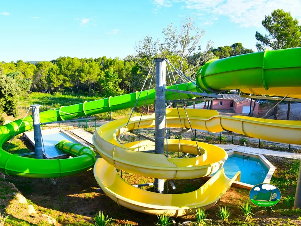 toboganes acuáticos verdes y amarillos en espiral con una piscina pequeña al fondo