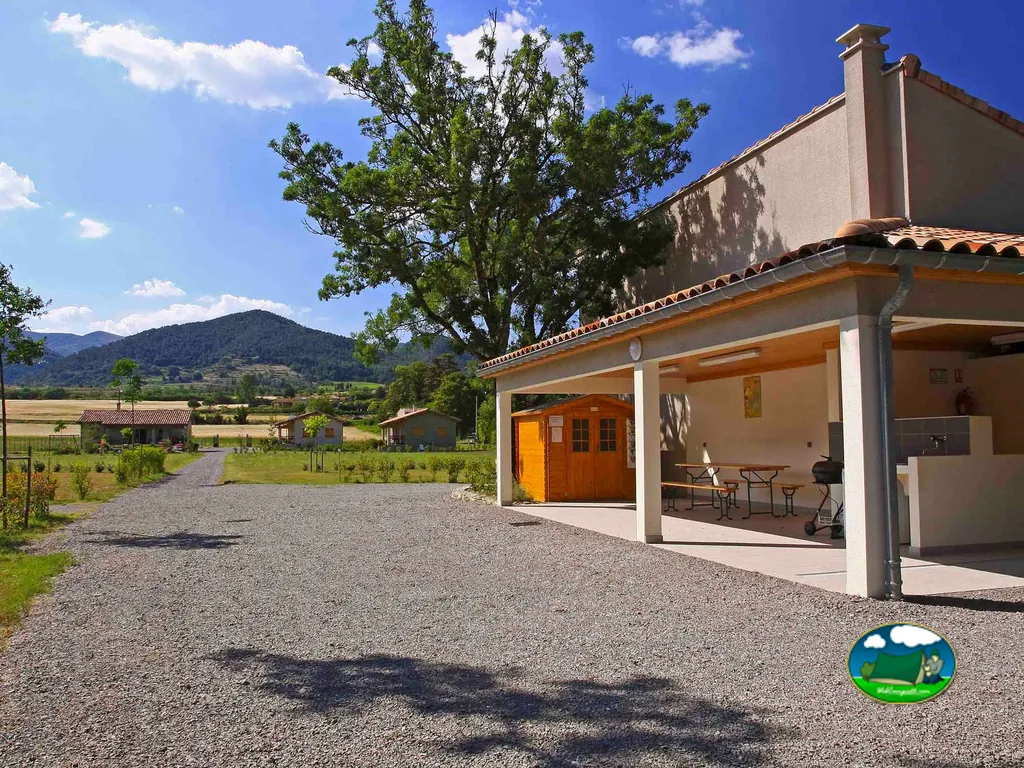porche con mesas de picnic y barbacoa junto a caseta de madera, con montañas al fondo
