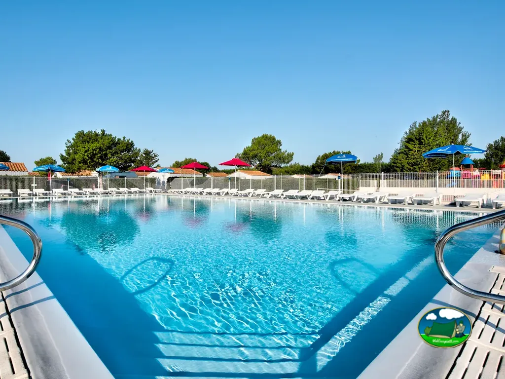 piscina rectangular con sombrillas de colores y tumbonas junto a los árboles