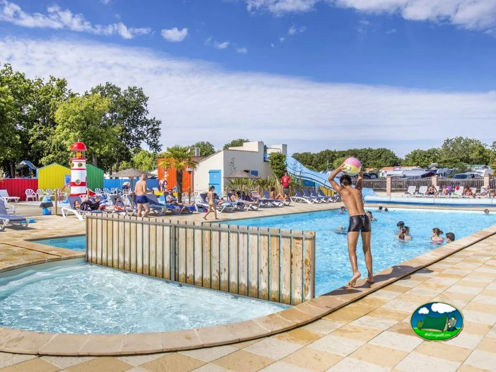 familia bañándose en la piscina con tobogán y el faro decorativo del parque infantil al fondo en Saint-Georges-d'Oléron