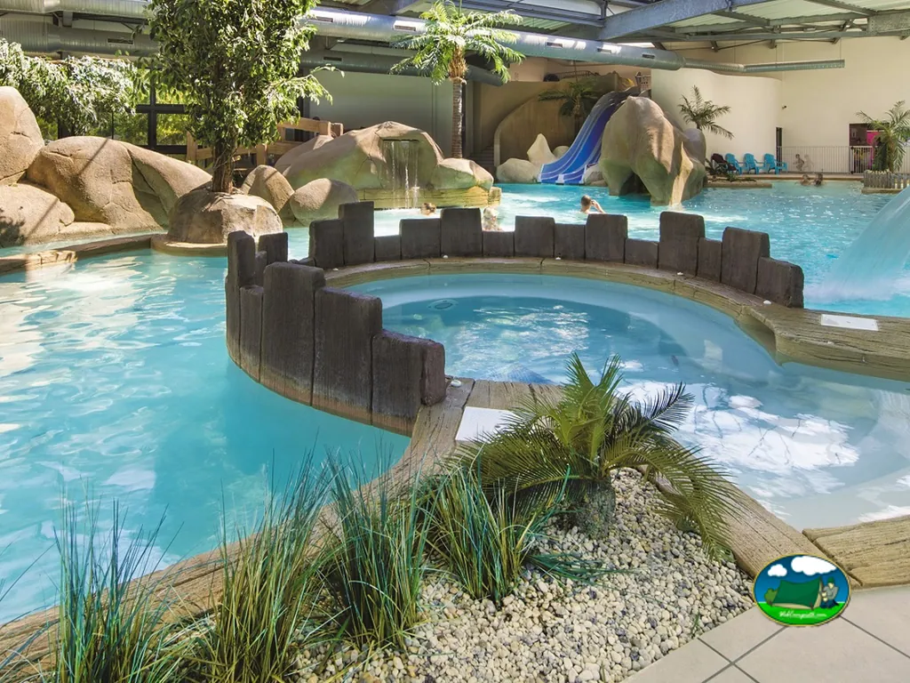 piscina cubierta con toboganes de roca artificial y jacuzzi en el parque acuático de Brem-sur-Mer