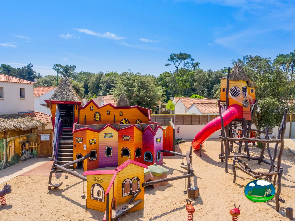 parque infantil temático de madera con torres y tobogán rojo entre árboles