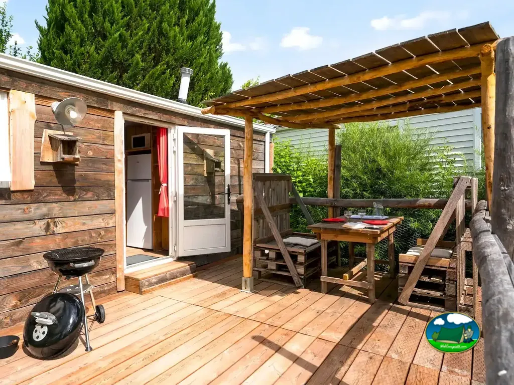 terraza de madera con barbacoa y mesa exterior de un bungalow en el camping de Saint-Hilaire-la-Forêt