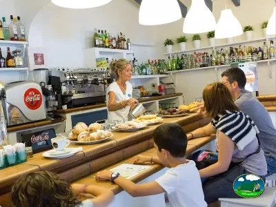 Restaurante bar con camarera sirviendo desayuno a clientes del Camping Son Bou, Alaior (Menorca)