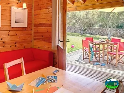 Cabaña con terraza, mesa y sillas rojas, vistas al jardín del Camping Son Bou, Alaior (Menorca)