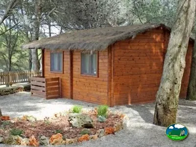Cabaña de madera con techo de paja entre árboles del Camping Son Bou, Alaior (Menorca)